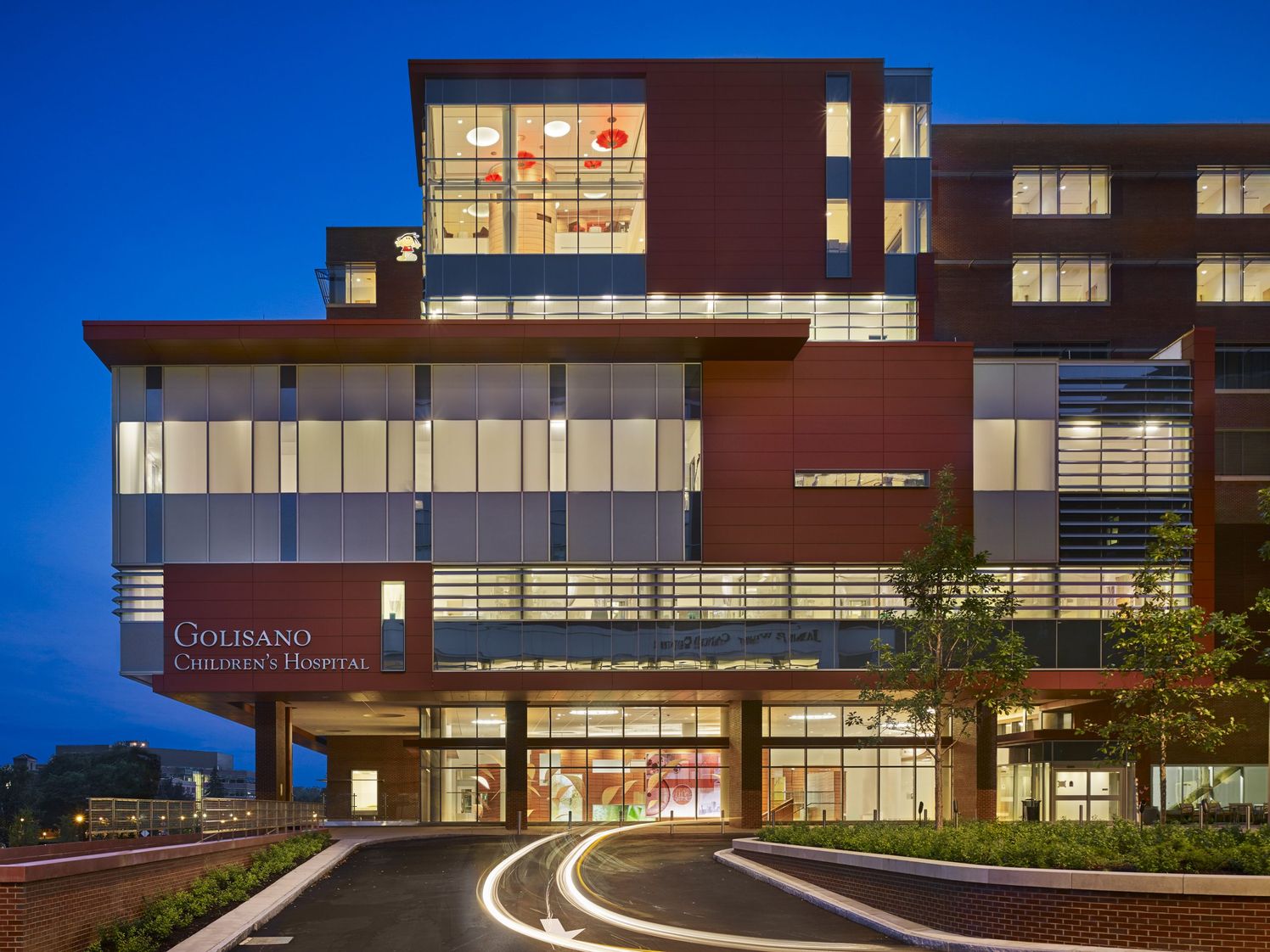 View at night of hospital entrance with lobby and atrium artwork visible through glowing windows