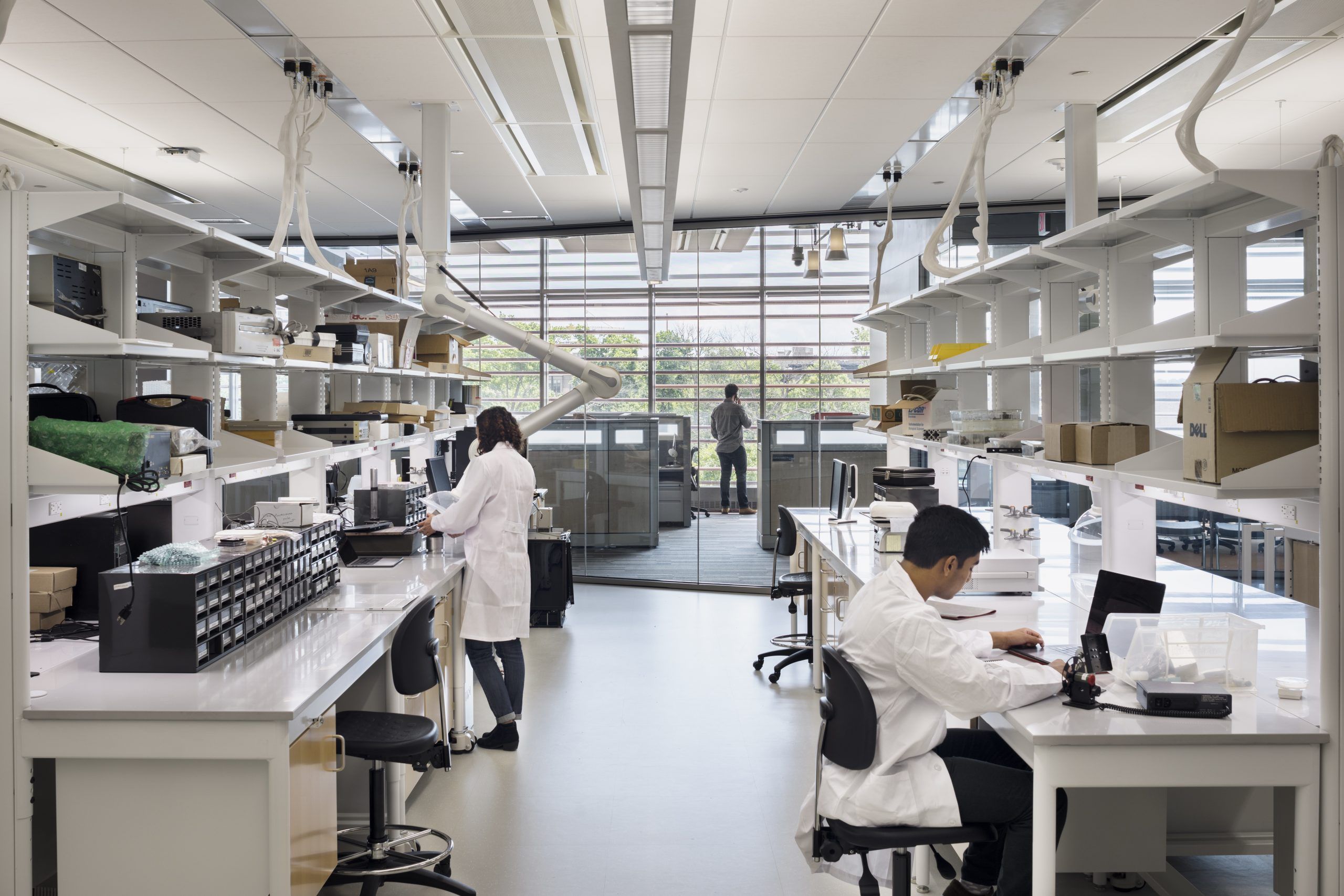 Students sitting at lab benches and standing at flexible lab banks with a glass wall in background