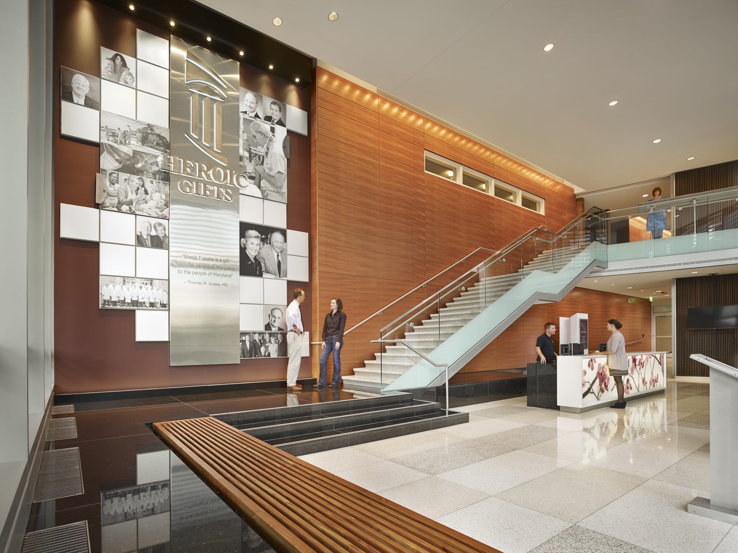 People chatting in the front lobby, with an information desk and wall of donor names leading up to the second floor balcony