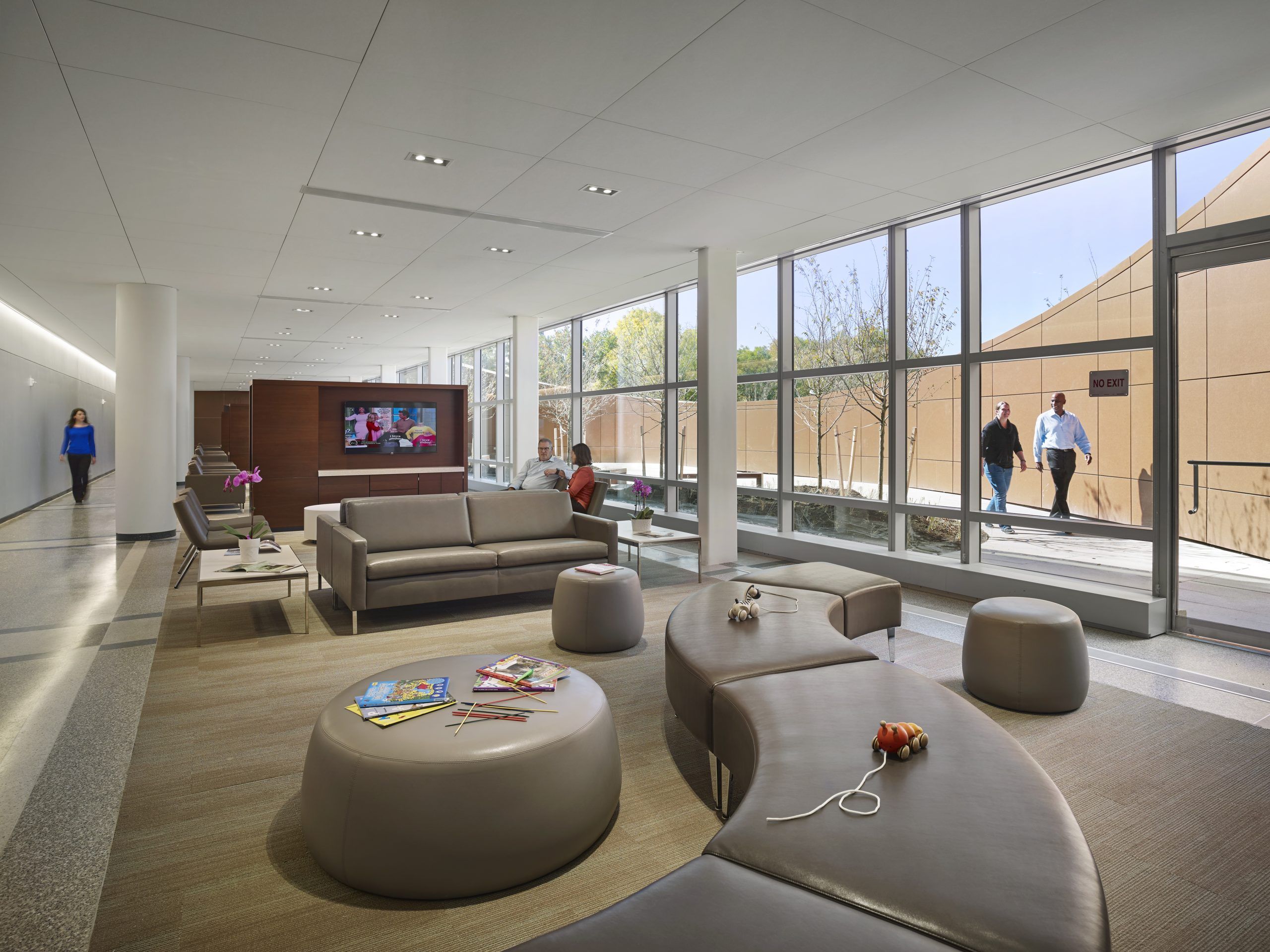 A lobby area with seating for families and children, television console, reading materials, and floor-to-ceiling windows opening onto a patio