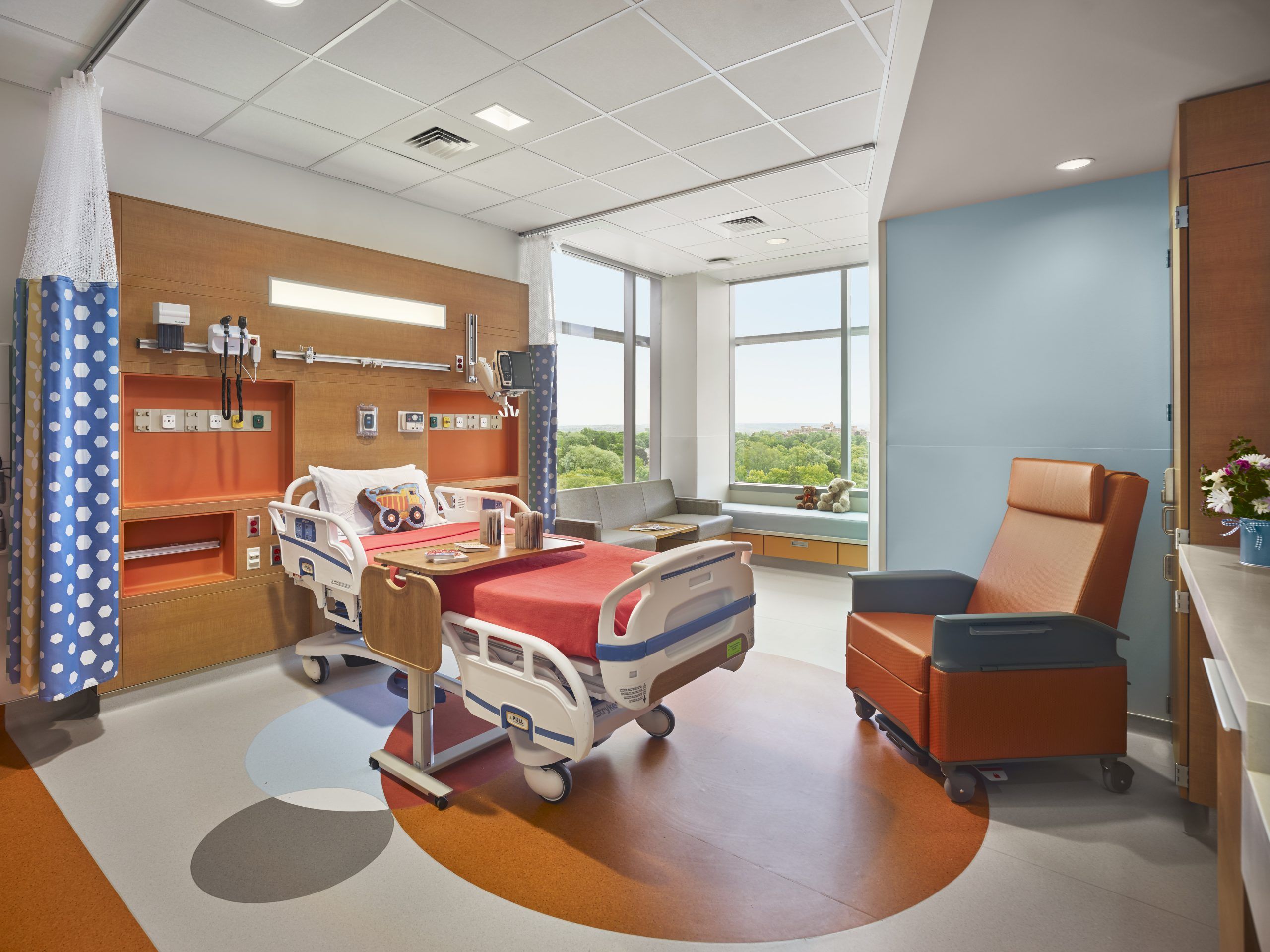 Pediatric patient room with red and blue train theming and long view out over medical campus