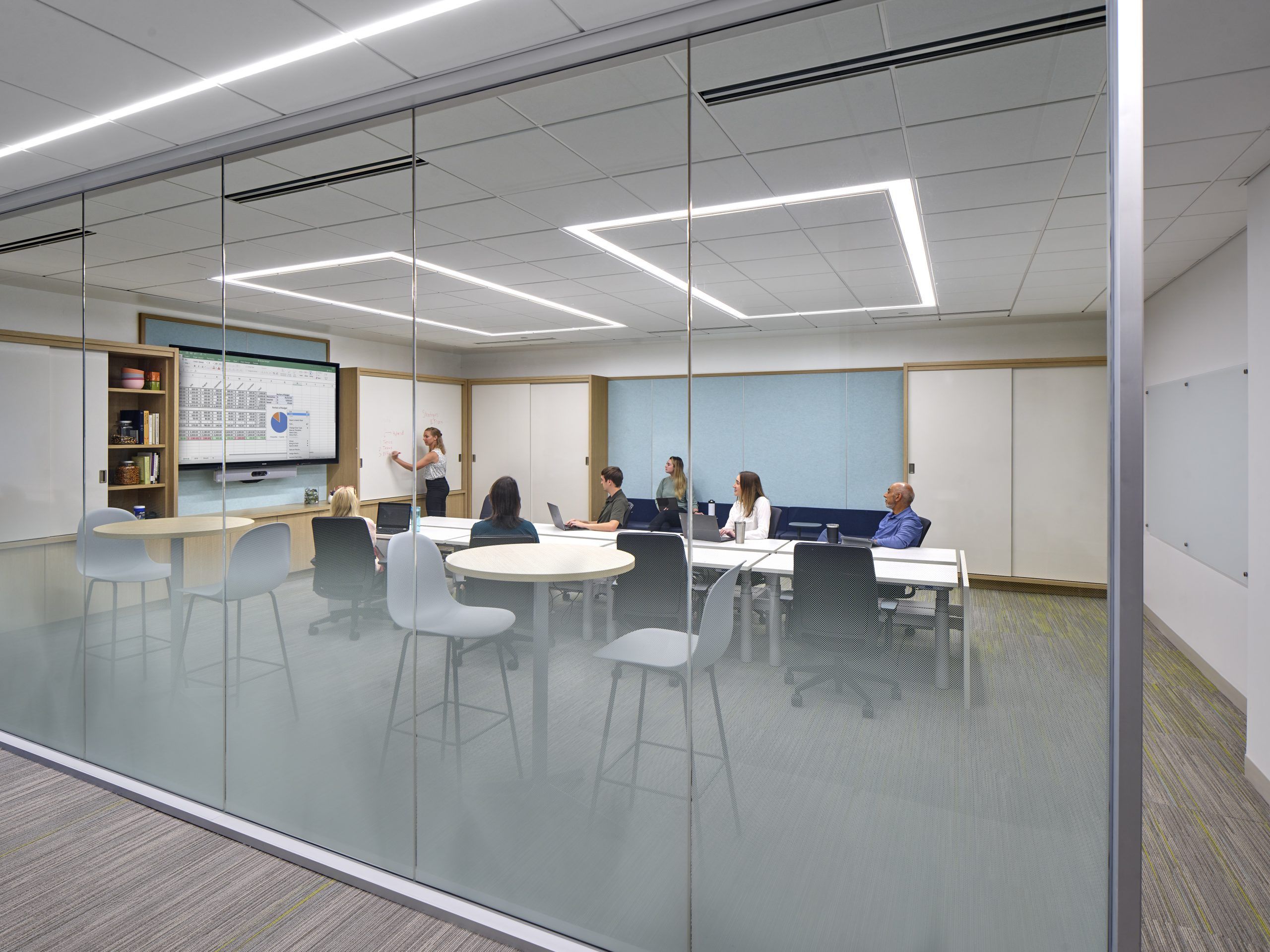 View from outside a meeting room with multiple tables and people working